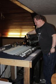 At Grace community ChurchRoger stands over a mixing table, messing with something out of sight behind a piece of equipment to his left. He is wearing jeans and a black shirt.